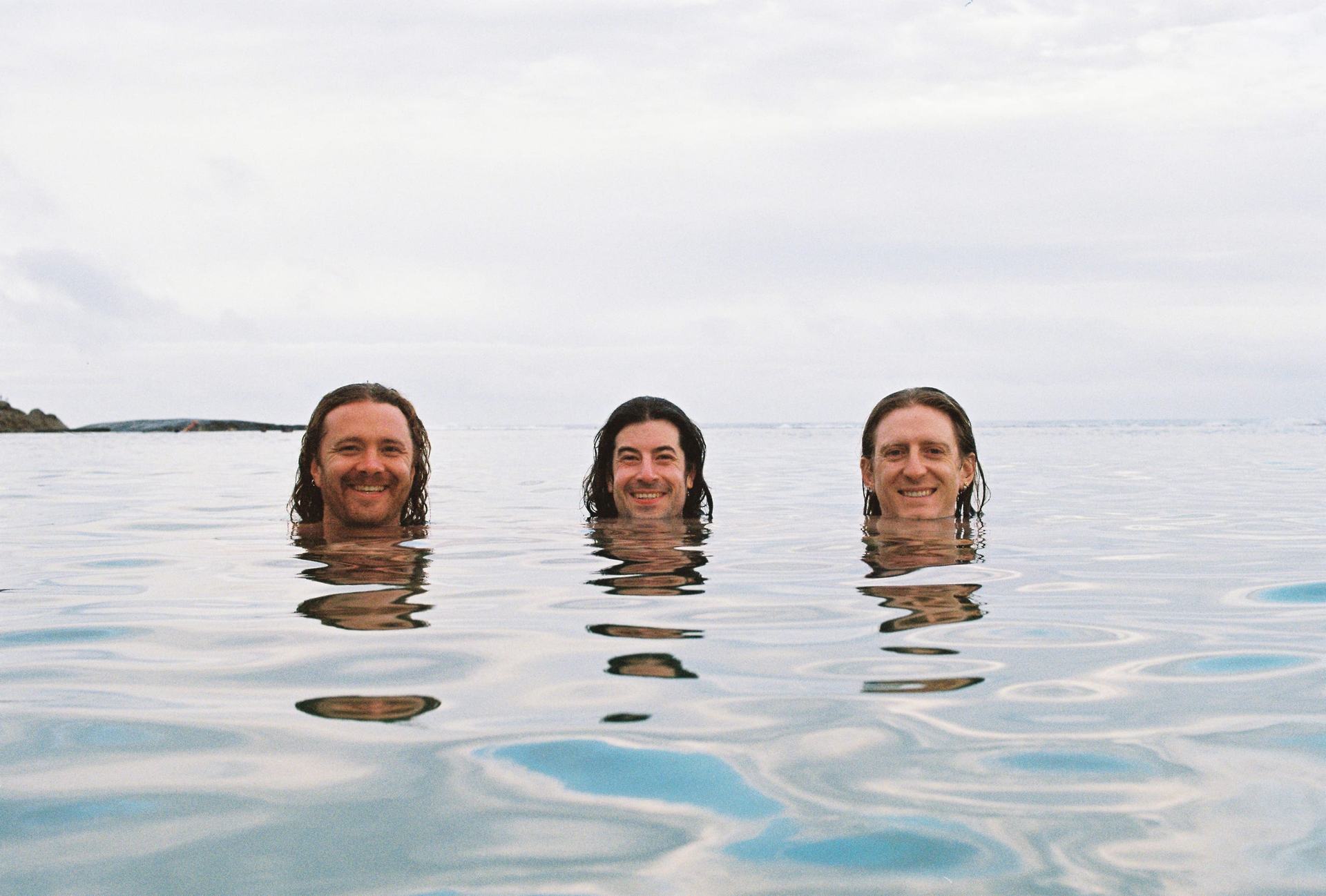 Three friends smiling with their heads just above the calm ocean water.